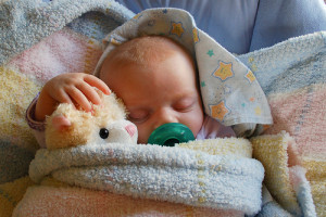 A baby happily sleeping with his pacifier.